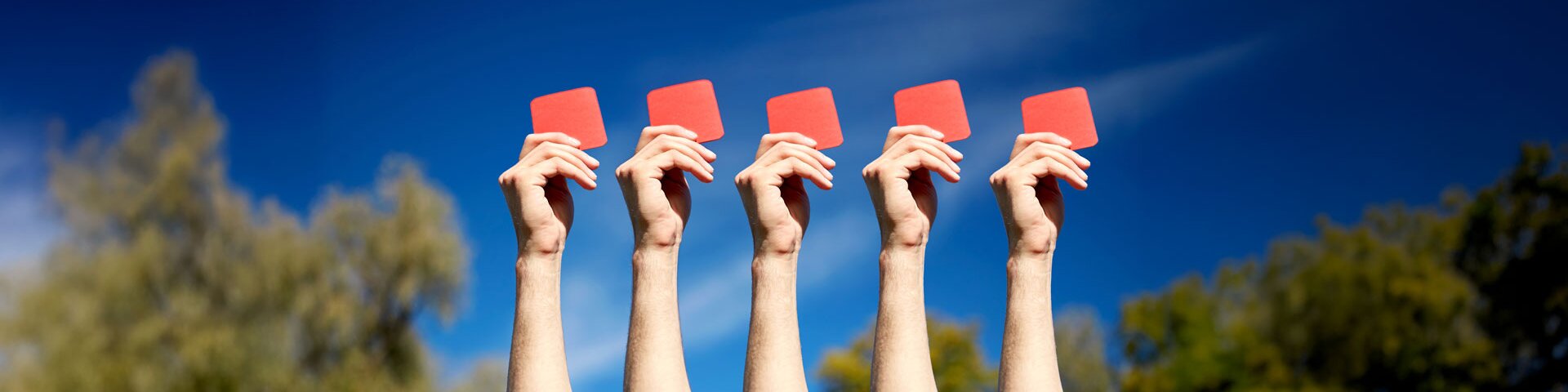Hände von fünf Personen, welche jeweils eine rote Karte hochhalten. Die Szene findet unter freiem Himmel statt. | © Foto: AdobeStock #141076083 | Syda Productions