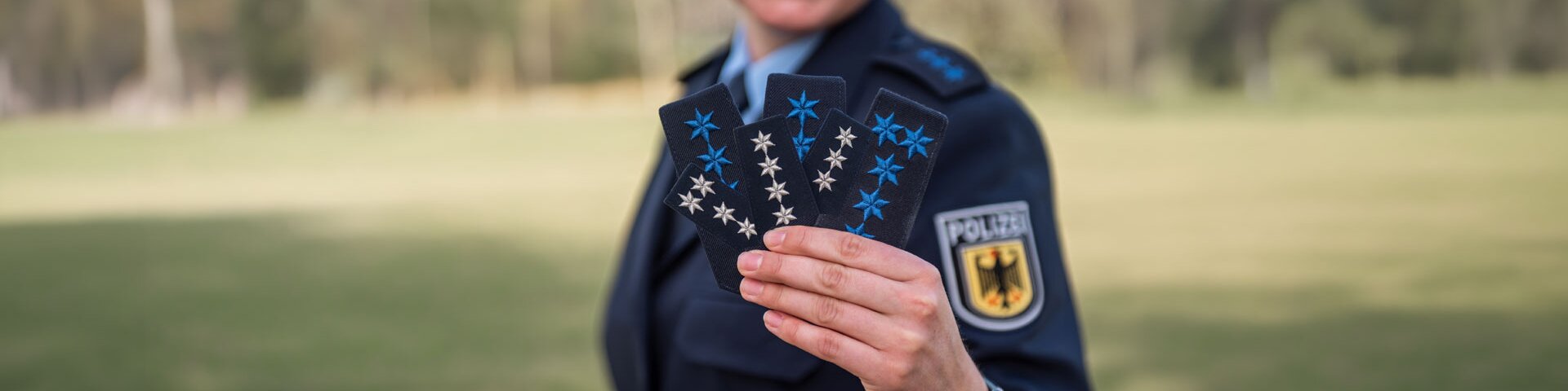 Eine Frau in Polizeiuniform hält mehrere Abzeichen in der Hand in Richtung Kamera | © Foto: GdP-Direktionsgruppe Bundesbereitschaftspolizei