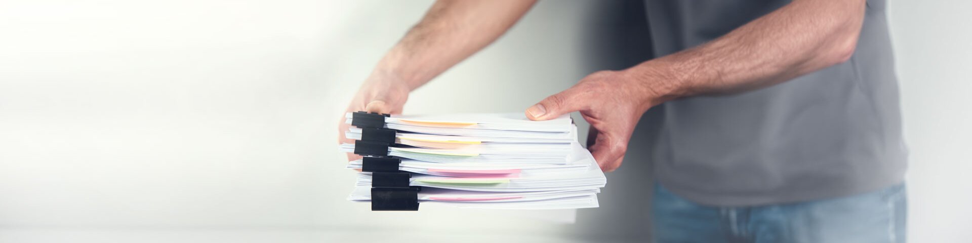 Eine Person legt einen Stapel gebündelter Papiere auf einen Tisch. | © Foto: AdobeStock #414536160 | ARAMYAN 