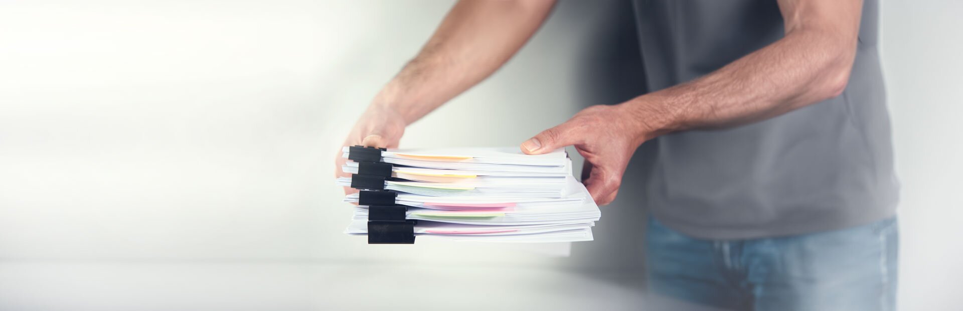 Eine Person legt einen Stapel gebündelter Papiere auf einen Tisch. | © Foto: AdobeStock #414536160 | ARAMYAN 