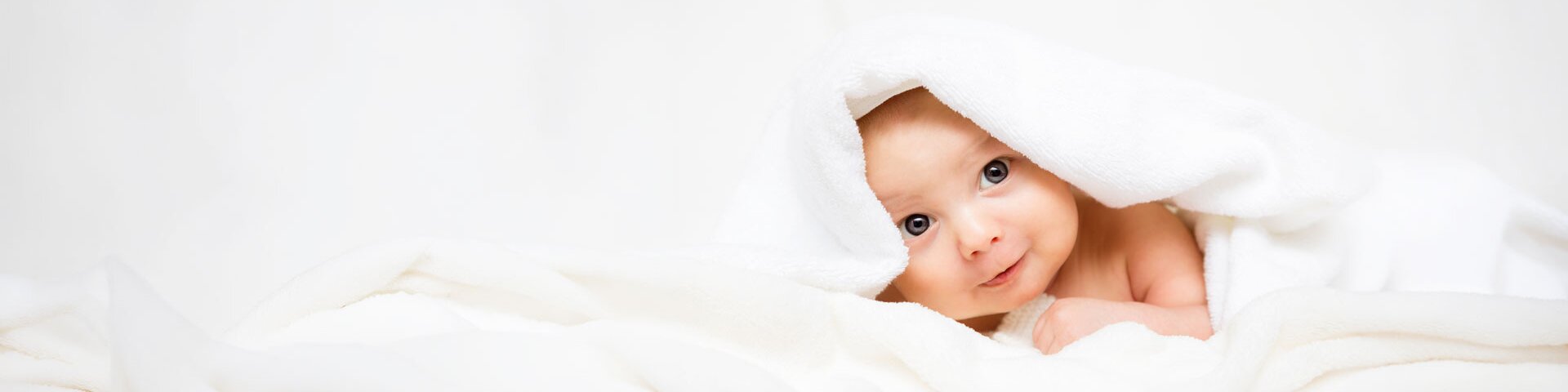 Ein Baby mit blaugrauen Augen liegt in einem weichen Handtuch eingewickelt auf einem Tisch. | © Foto: AdobeStock #171484206 | ballabeyla